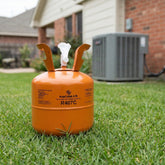 Orange refrigerant canister on grass with air conditioning unit in the background